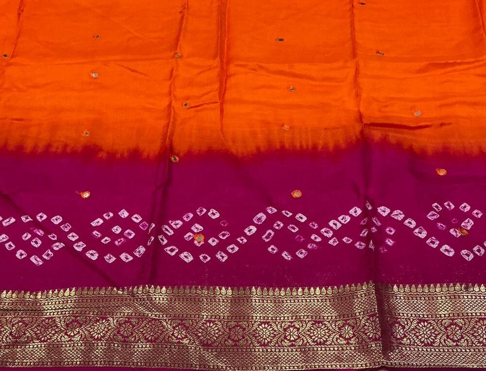 Pure crape silk saree with zari woven border and rich pallu. Hand tied bhandani with two color shaded dying. Cotton tassles on apllu. Running blouse with aari mirror work. Saree- 5.5 meters. Blouse- 1 meter.